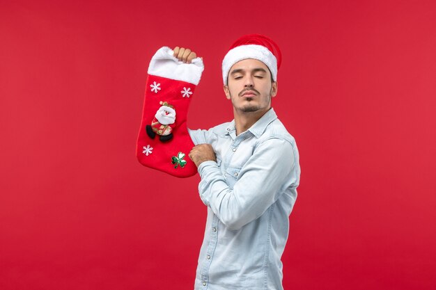 Вид спереди молодого человека с рождественским носком на красной стене