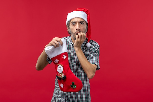 Front view of young man with christmas sock on a red wall