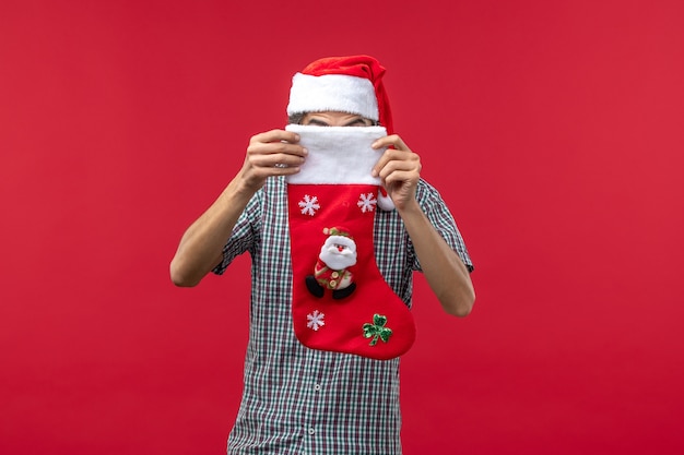 Front view of young man with christmas sock on a red wall