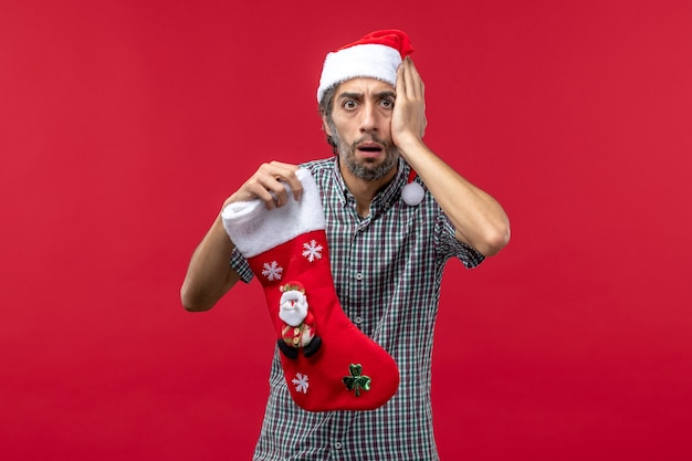赤い壁にクリスマスの靴下を持つ若い男の正面図