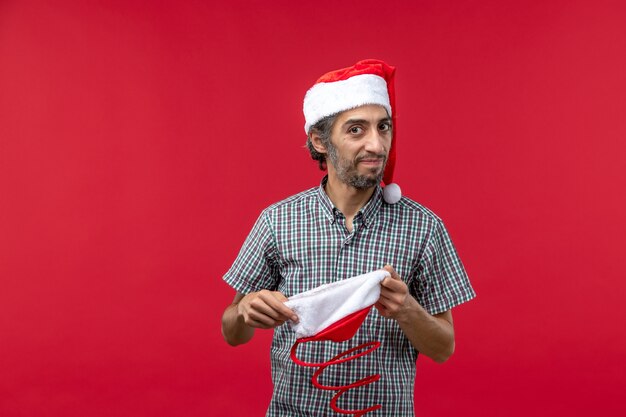 Вид спереди молодого человека с рождественской игрушкой на красной стене