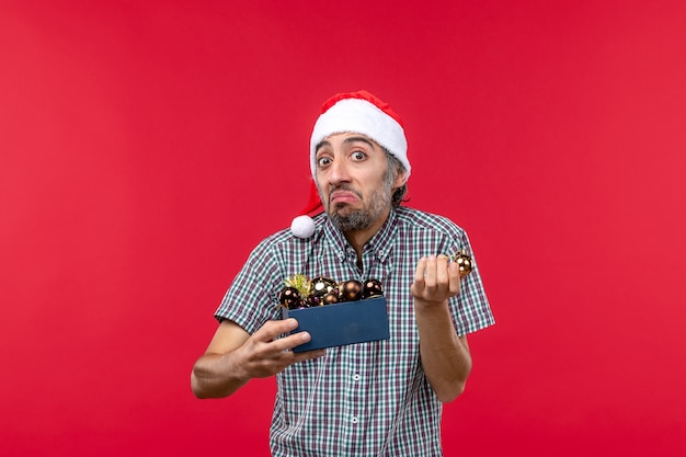 Free photo front view young man with christmas tree toys on red desk