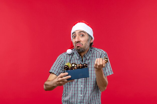 Front view young man with christmas tree toys on red desk