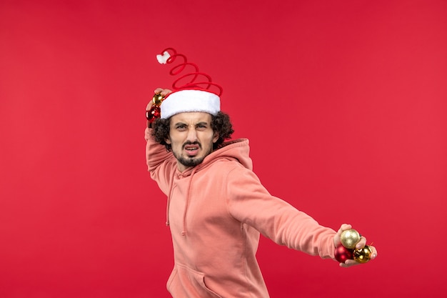 Free photo front view of young man with christmas tree toys on a red wall