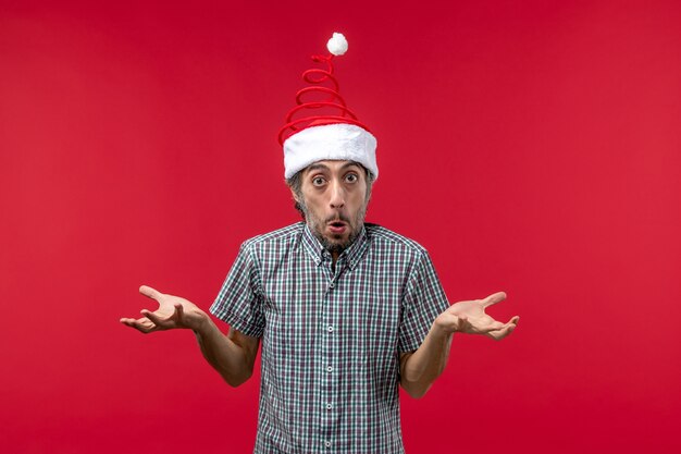 Front view of young man with confused expression on red wall