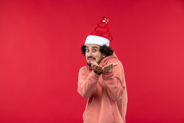 Front view of young man with confused expression on red wall