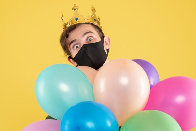 無料写真 正面図黄色の風船を保持している王冠と黒のマスクを持つ若い男
