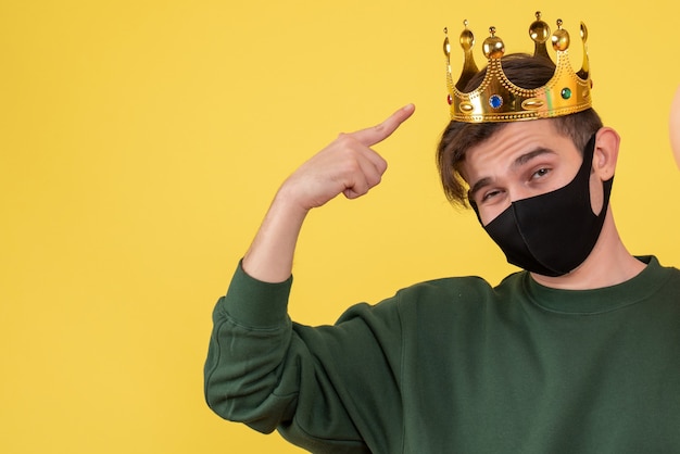 Free photo front view young man with crown and black mask pointing at his crown on yellow