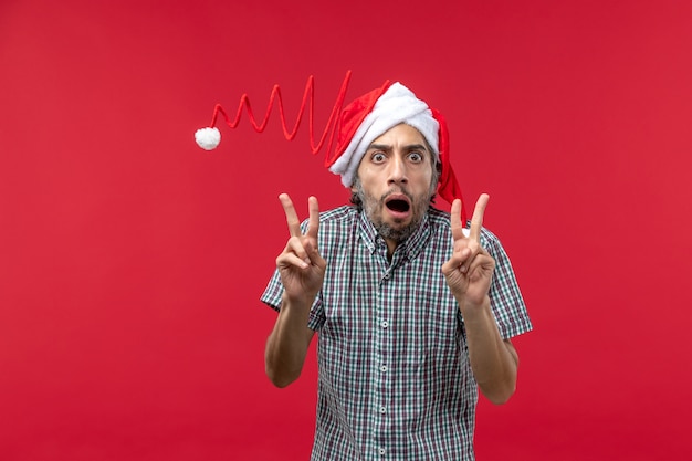 Front view of young man with funny toy cap on a red wall
