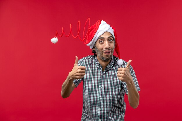 Front view of young man with funny toy cap on red wall