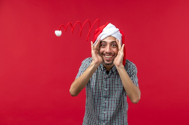 Front view of young man with funny toy cap on red wall