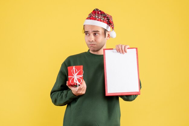 녹색 스웨터 선물 및 클립 보드 노란색에 서있는 전면보기 젊은 남자