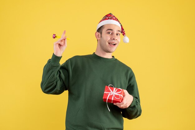 Front view young man with green sweater holding noisemaker standing on yellow 