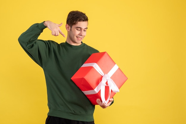 Front view young man with green sweater pointing at gift on yellow 