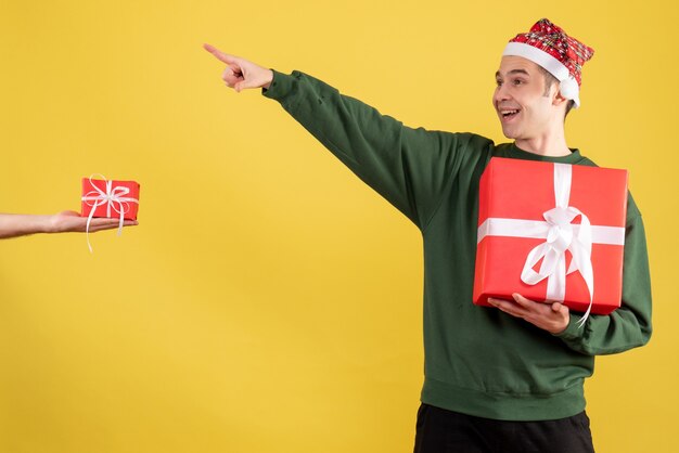 Front view young man with green sweater pointing at something standing human hand holding gift on yellow 