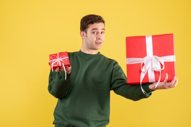 노란색에 서있는 선물을 보여주는 녹색 스웨터와 전면보기 젊은 남자