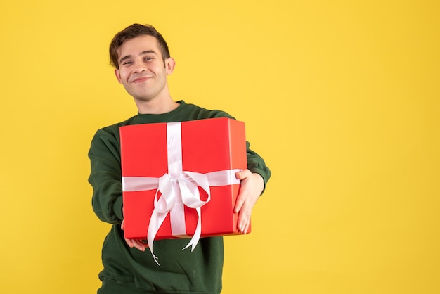 Front view young man with green sweater showing his gift on yellow 