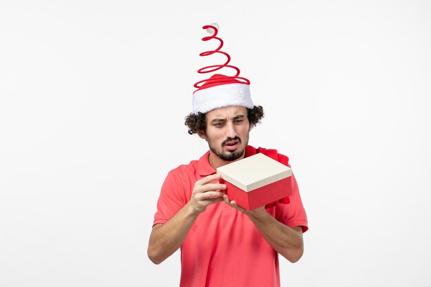 Front view of young man with holiday present on white wall