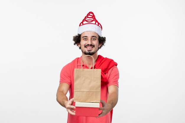 Front view of young man with holiday presents on the white wall