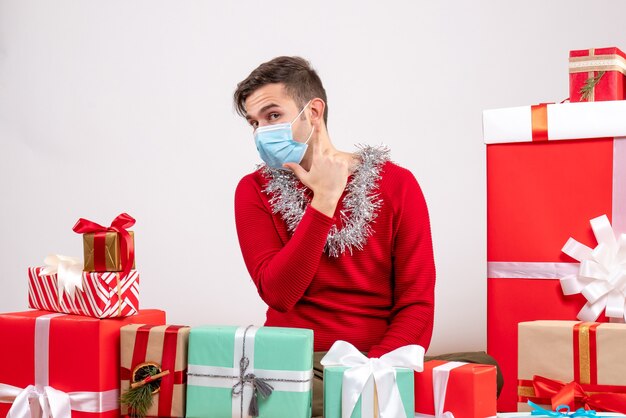 Front view young man with mask making finger gun sitting around xmas gifts