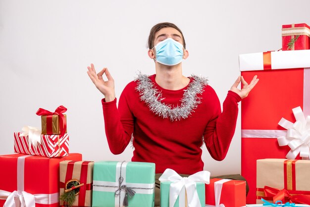 Front view young man with mask making meditation sign sitting around xmas gifts