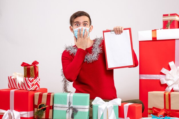 Front view young man with mask putting hand to his face sitting around xmas gifts