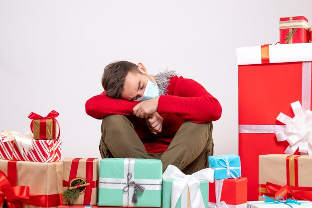 Front view young man with mask sleeping around xmas gifts