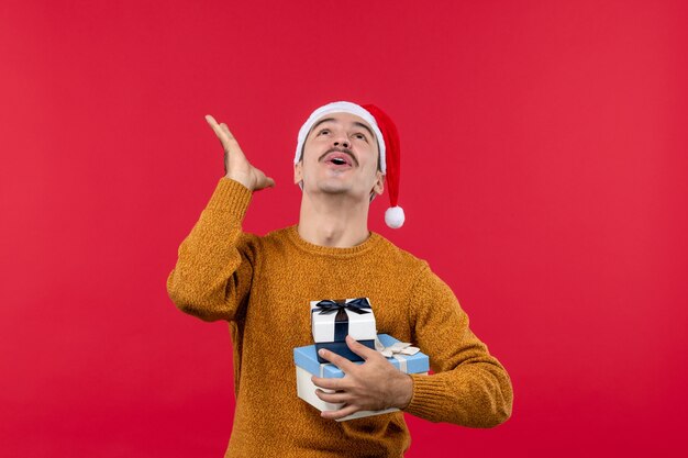 Front view of young man with new year presents on a red wall