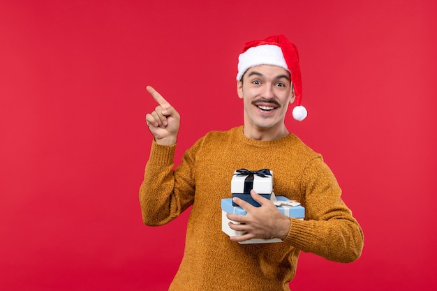 Вид спереди молодого человека с новогодними подарками на красной стене