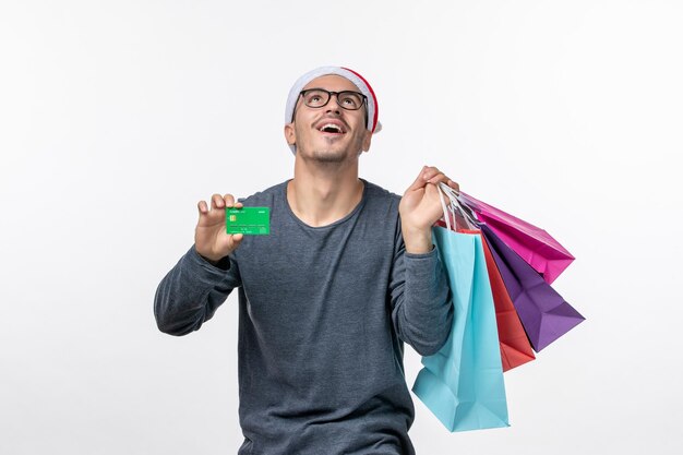 Front view of young man with packages and bank card on white wall