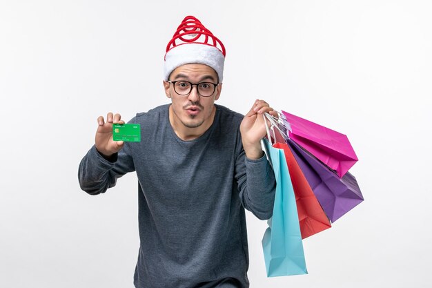 Front view of young man with packages and bank card on white wall