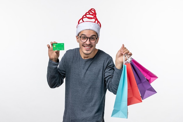 Front view of young man with packages and bank card on white wall