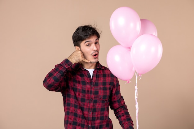 Вид спереди молодой человек с розовыми воздушными шарами на коричневой стене