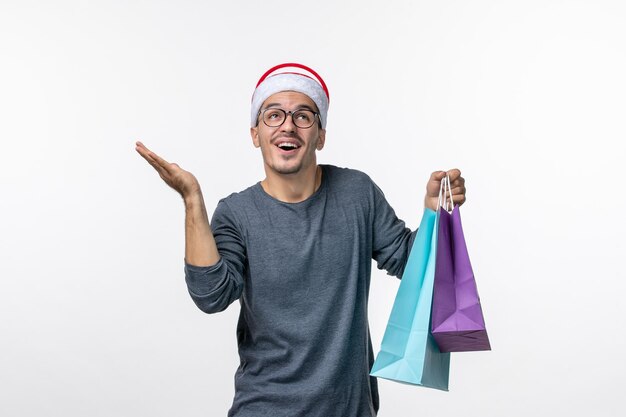 Front view of young man with presents after shopping on white wall