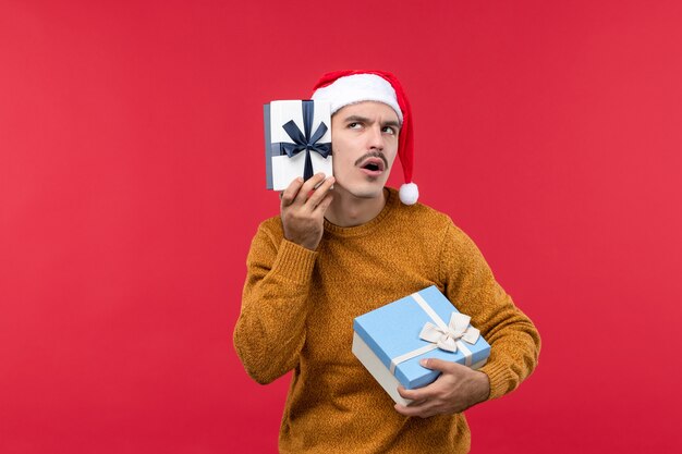 Front view of young man with presents on red wall