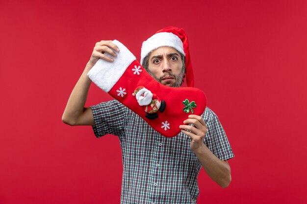 Front view of young man with red christmas sock on red wall