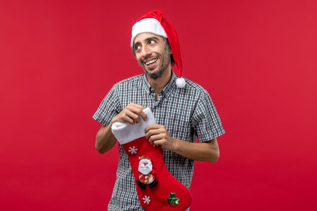 Вид спереди молодого человека с красным рождественским носком на красной стене