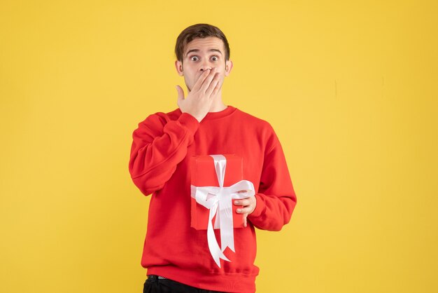 Front view young man with red sweater covering his mouth on yellow background