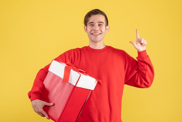 Front view young man with red sweater finger pointing up on yellow background