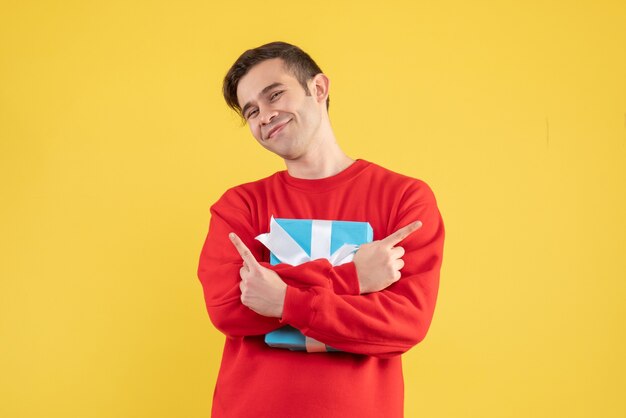 Front view young man with red sweater holding his gift tight on yellow background