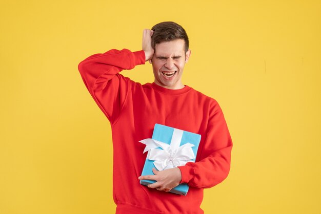 Front view young man with red sweater holding his head on yellow background