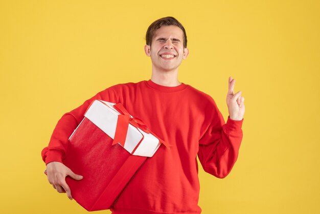 노란색 배경에 행운을 빌어 요 기호를 만드는 빨간 스웨터와 전면보기 젊은 남자