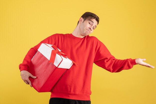 Front view young man with red sweater opening his hand on yellow background