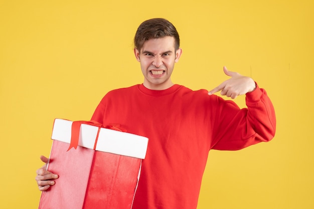黄色の背景に自分自身を指している赤いセーターと正面図の若い男