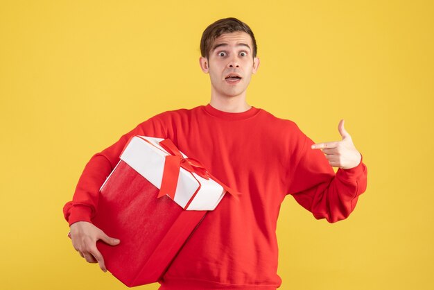 Front view young man with red sweater pointing at himself on yellow background