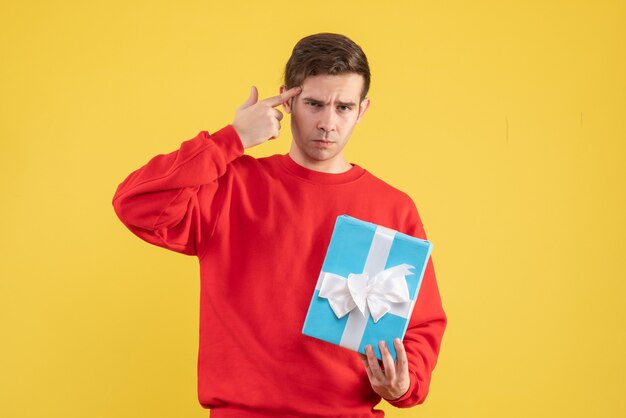 Front view young man with red sweater putting finger gun to his temple on yellow background