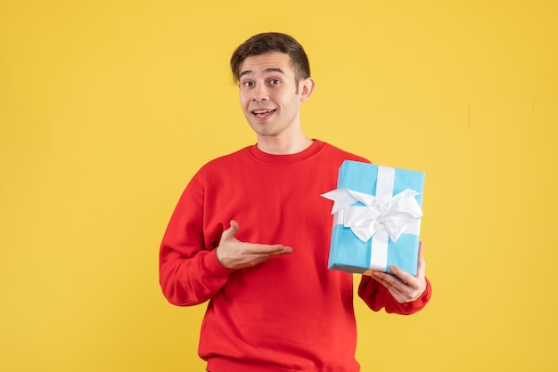 Front view young man with red sweater showing his gift on yellow background