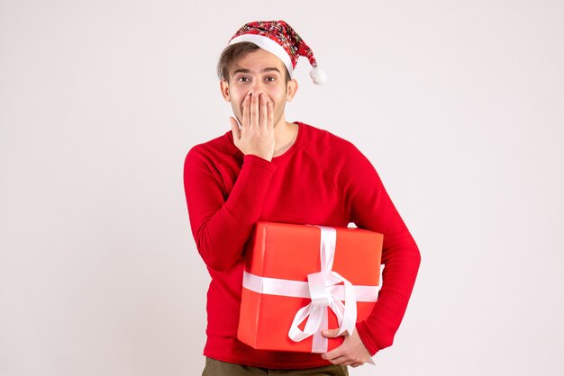 Front view young man with santa hat covering his mouth on white background