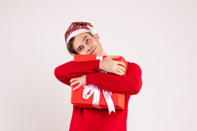 Front view young man with santa hat holding tightly his gift on white background