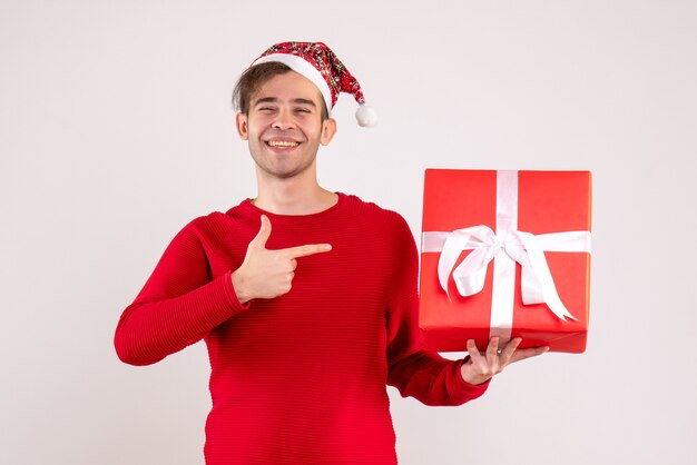 Front view young man with santa hat pointing at gift on white background